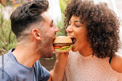 Diverse couple biting burger together
