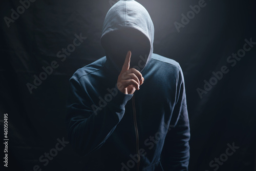 the hacker in the hood makes a silence gesture photo