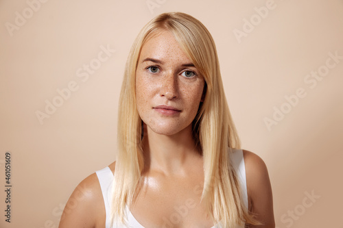 Portrait of young blond woman with freckles standing in a studio looking straight of a camera