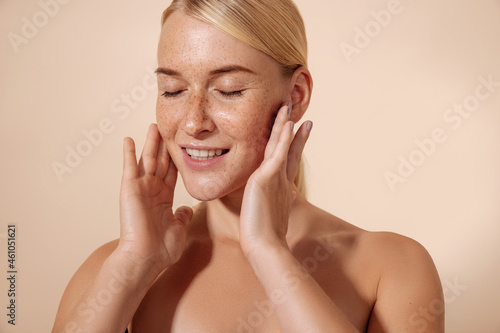 Young smiling woman massaging her face with fingers standing in studio with closed eyes