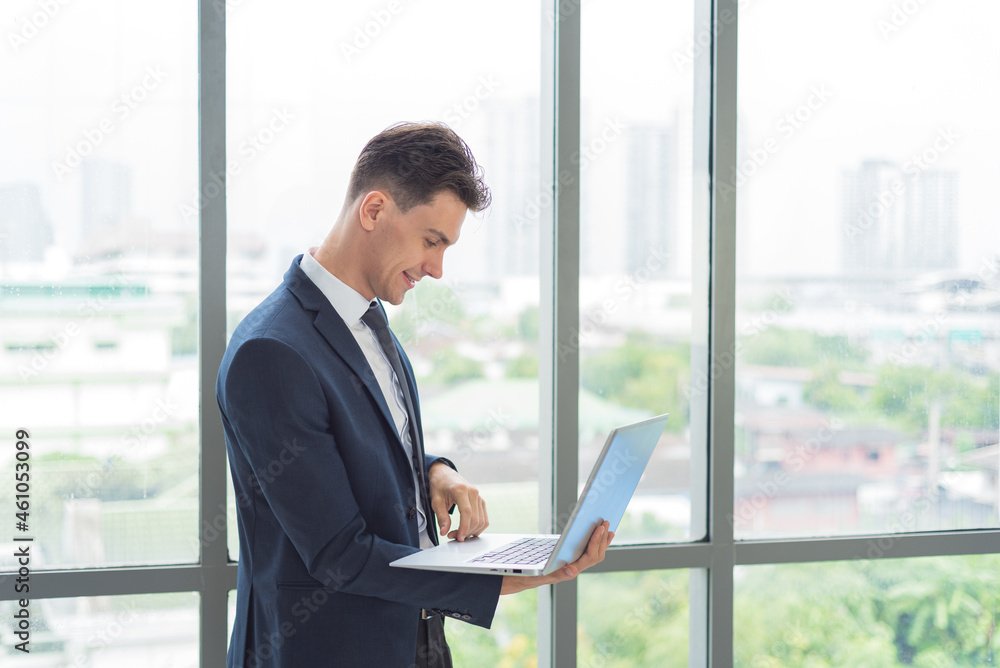 Portrait of adult smart business man in suit outfit standing and using laptop in modern workplace
