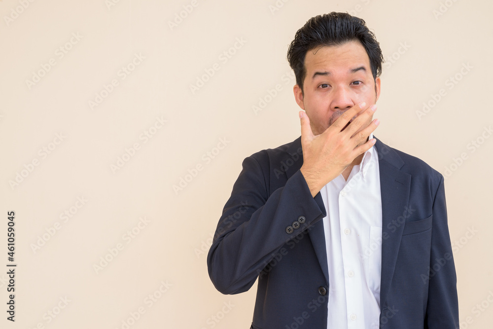 Portrait of Asian businessman wearing suit against plain background while looking shocked Portrait of Asian businessman wearing suit against plain background while looking shocked