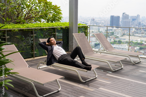 Murais de parede Asian businessman wearing suit and relaxing outdoors while laying down on sunbed