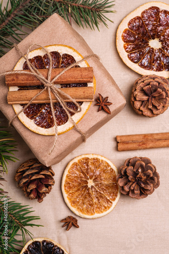 Fototapeta Naklejka Na Ścianę i Meble -  Christmas composition with handmade kraft paper gift box, dried citrus slices, cinnamon, anise, pine cones and fir tree branches, top view close up