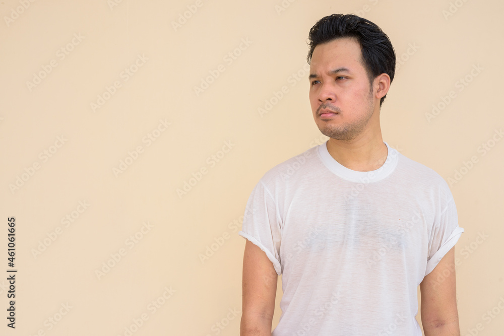 Portrait of Asian man wearing white t-shirt against plain background outdoors while thinking Portrait of Asian man wearing white t-shirt against plain background outdoors while thinking