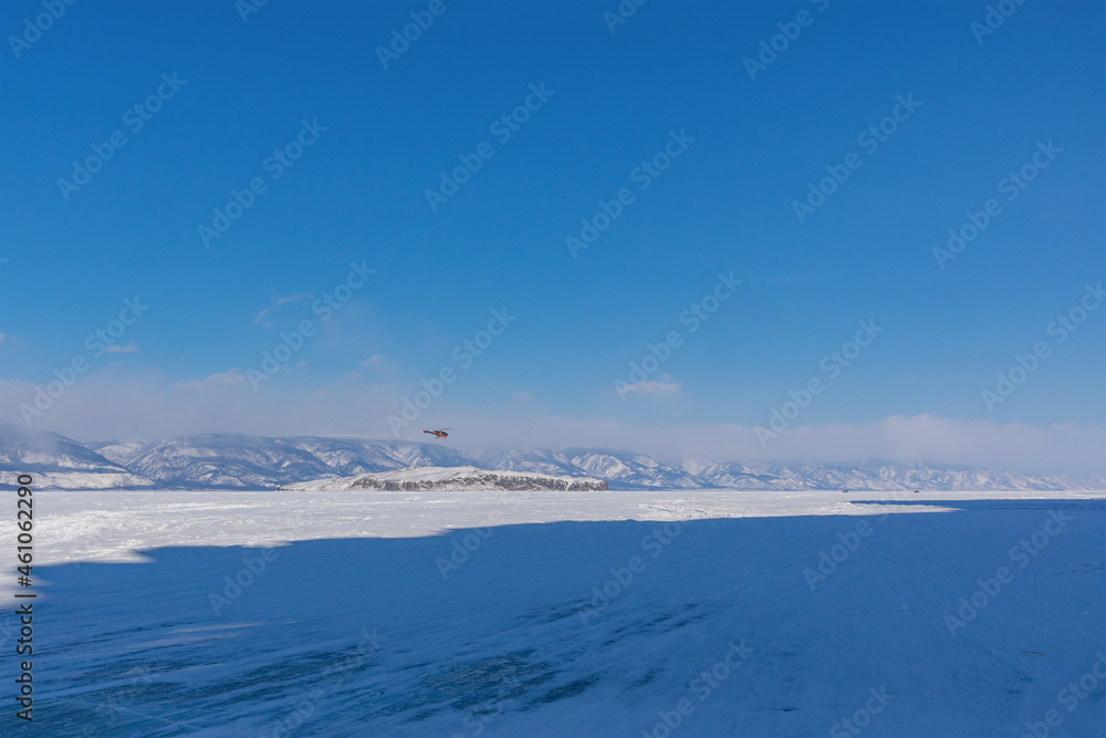 Snow-covered ice of Baikal in the Maloye More Strait near Olkhon Island against the background of mountains. Winter landscape on a sunny day. Natural background