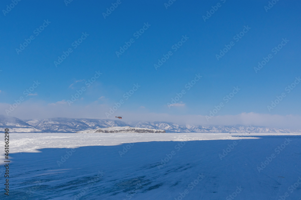 Obraz premium Snow-covered ice of Baikal in the Maloye More Strait near Olkhon Island against the background of mountains. Winter landscape on a sunny day. Natural background