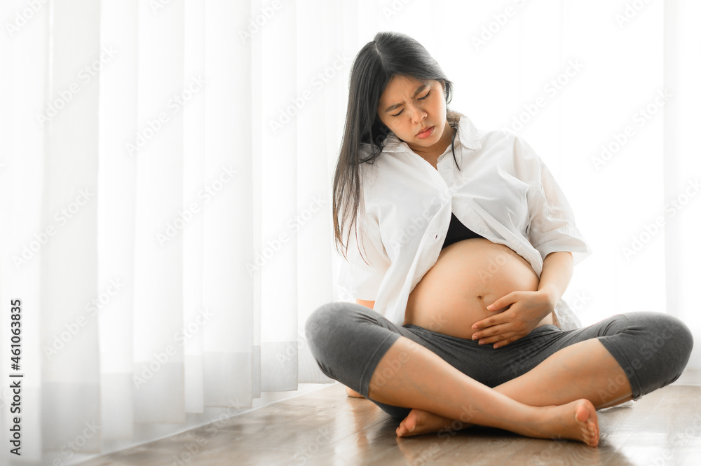 Asian pregnant woman touch her tummy feeling hurt and stomachache while sitting on the floor Asian pregnant woman touch her tummy feeling hurt and stomachache while sitting on the floor