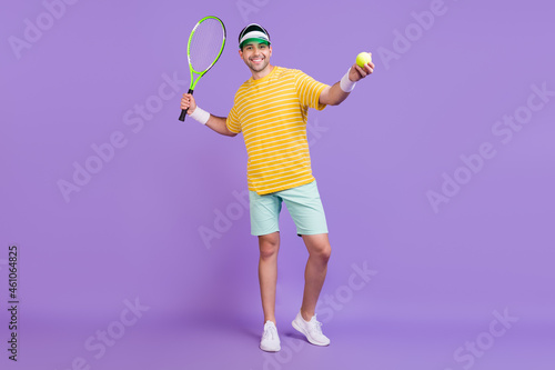 Full length photo of cheerful young happy man hold ball racket tennis player isolated on purple color background