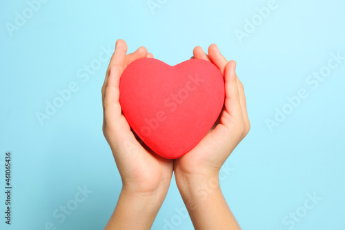 Red heart in children's hands on a blue background close up