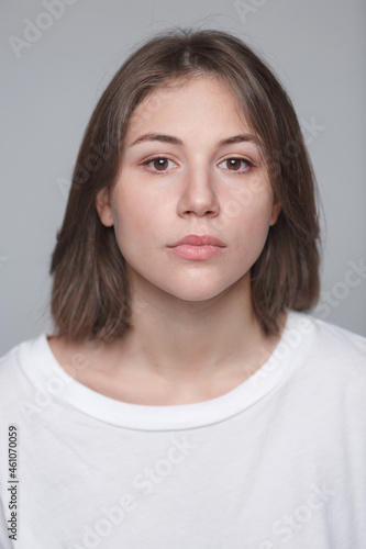 Portrait of a young woman 27 years old, she is looking at the camera. Natural look, fresh skin. White T-shirt and gray background.