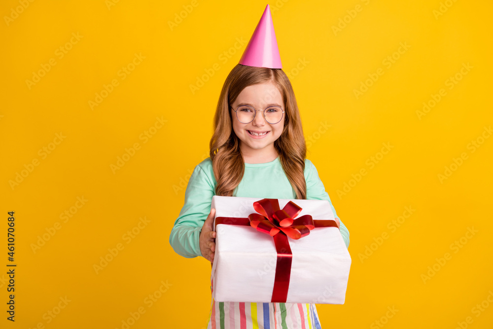 Photo of cute sweet schoolgirl dressed turquoise shirt spectacles cap smiling holding present box isolated yellow color background Photo of cute sweet schoolgirl dressed turquoise shirt spectacles cap smiling holding present box isolated yellow color background
