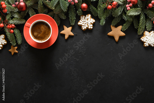 Christmas frame with coffee, festive cookies, evergreen branches, red holly balls on black background. Xmas greeting card. Holiday winter time. Happy New Year. Space for text. View from above. © svetlana_cherruty