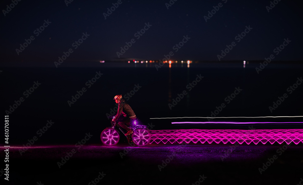 Bicycler riding along sea and leaving light trails at night