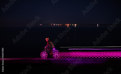 Bicycler riding along sea and leaving light trails at night 