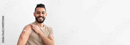 Cheerful Arab man showing arm with band aid after receiving covid vaccine injection  smiling  feeling protected