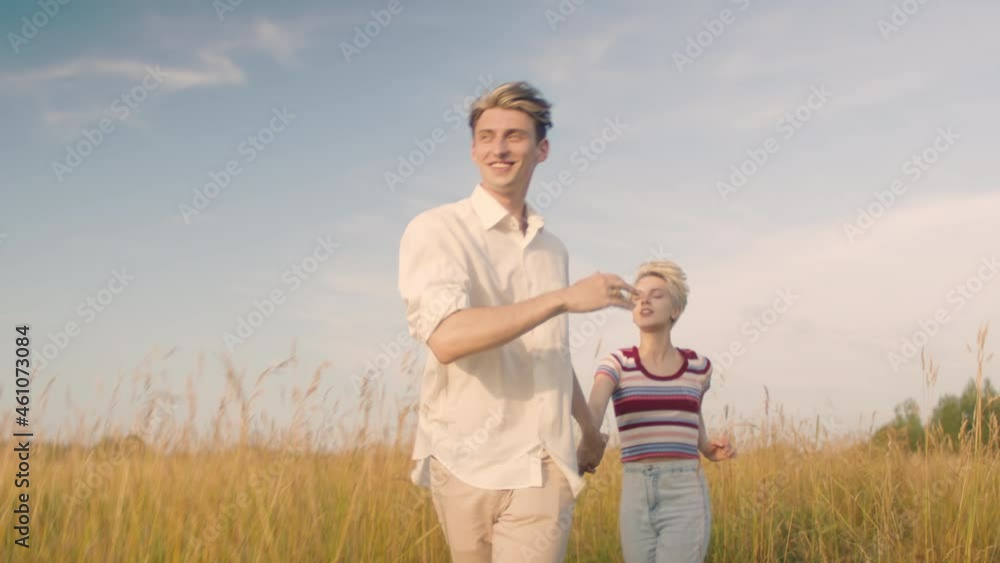 Candid and real young couple run in field. Cinematic warm summer shot of forever youth vibes. Couple in love run towards camera through field of gold wheat. Relationship goals concept Candid and real young couple run in field. Cinematic warm summer shot of forever youth vibes. Couple in love run towards camera through field of gold wheat. Relationship goals concept