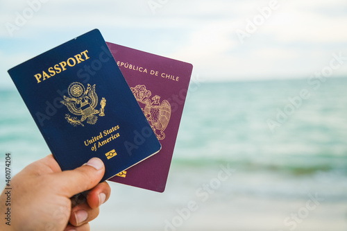 a hand holding two passport a red and a blue one on a beach