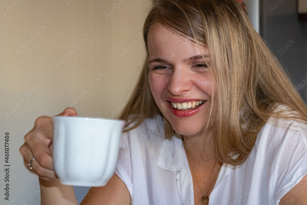 A smiling and in a good mood young woman with long blond hair holding a cup of coffee in her hand A smiling and in a good mood young woman with long blond hair holding a cup of coffee in her hand