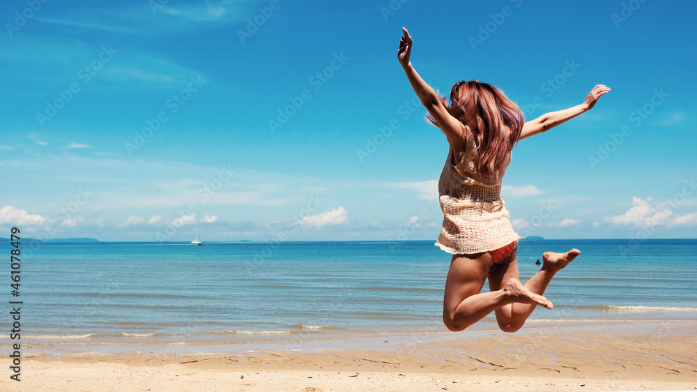 Happy asian young woman in casual style fashion jumping at sand beach. Relaxing, fun, and enjoy holiday at tropical paradise beach with blue sky and white clouds. Girl in summer vacation.
