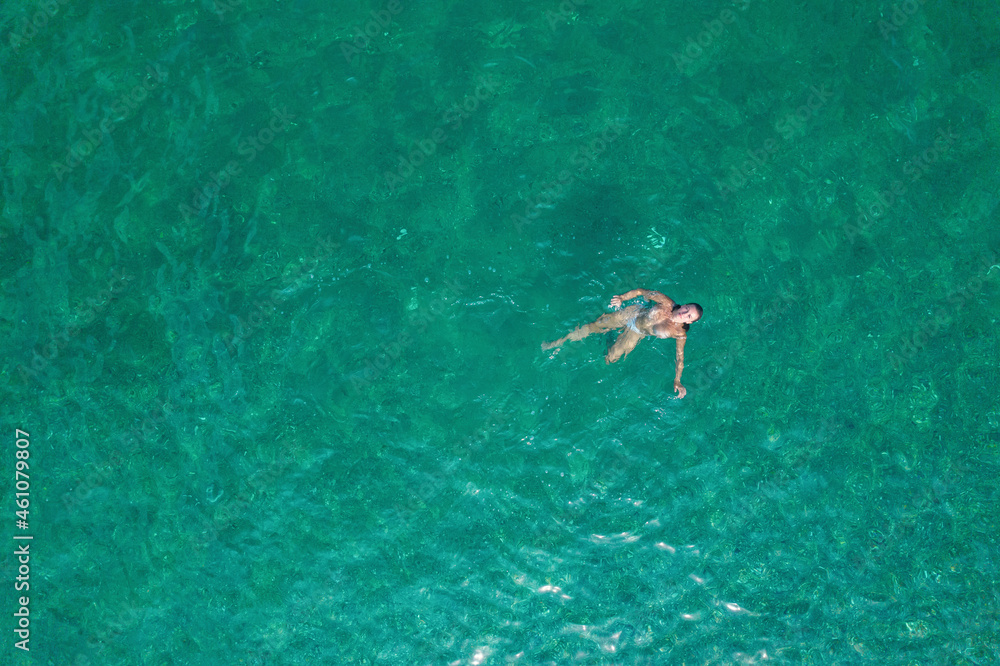 Young nude beautiful, sexy woman with naked breast taking off swimsuit standing in sea, ocean water. Summer. View from above. Top view, copter