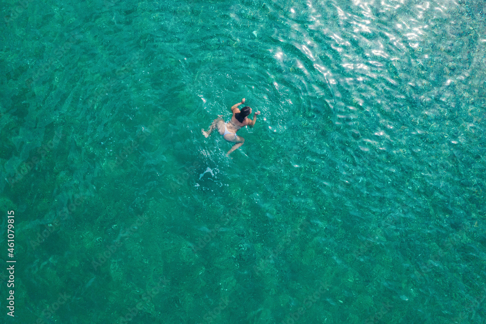 Young woman in a swimsuit swimming in sea water on the beach. View from above. Top, drone view