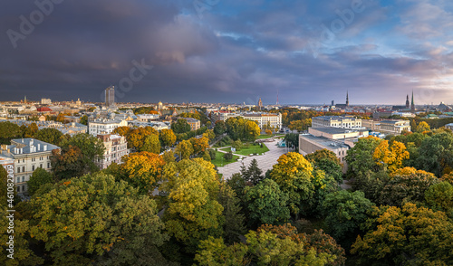 Park in Riga with trees in autumn colors. Colorful sunset over the city panorama. Downtown in background. © Viesturs
