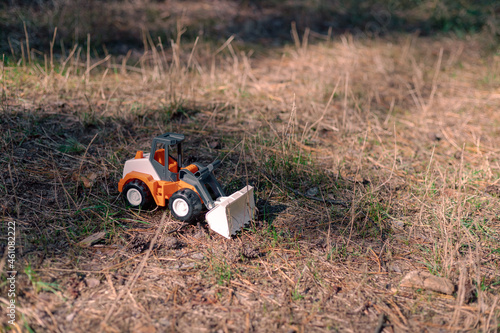 Toy tractor in dry grass. Orange plastic tractor on dry pine needles in the forest