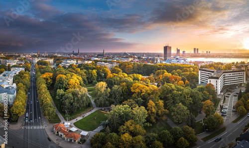 Park in Riga with trees in autumn colors. Colorful sunset over the city panorama. Downtown in background. photo