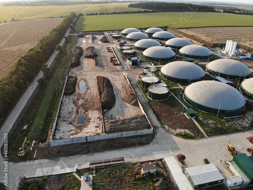 Biogas complex on nature landscape. Agricultural plant for biomass production on green field. Modern storage for renewable energy.