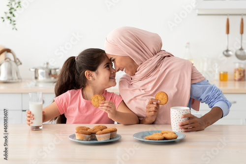 Schilderij op canvas Happy Muslim Mom And Her Little Daughter Eating Snacks In Kitchen Together