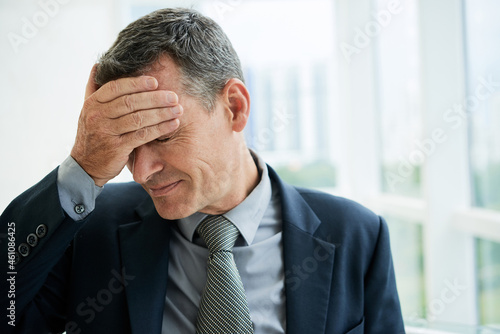 Tired or dissappointed mature male executive in necktie touching forehead while feeling headache or elevated temperature photo