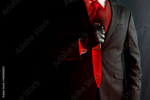 Portrait of Businessman in Black Suit and Red Tie Holding Bloody Red Knife on Black Background. Halloween Horror Movie Killer Concept.  photo