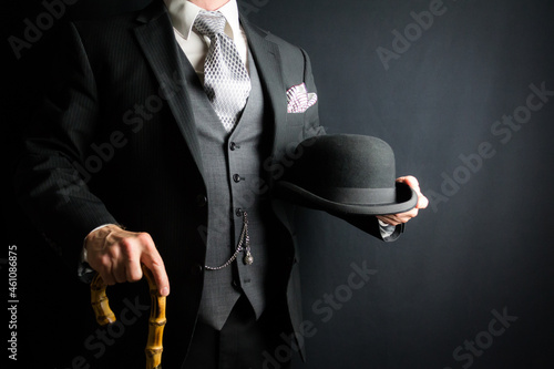 Fotografi Portrait of Man in Dark Suit Holding Bowler Hat and Umbrella on Black Background