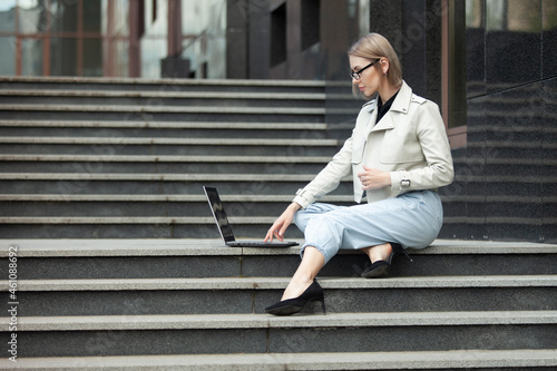 Modern business lady sitting on the stairs with laptop near the business center. Freelance, Remote Work, Lifestyle
