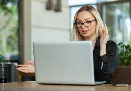 Business woman makes videoconference while sitting at the table with laptop in outdoor cafe