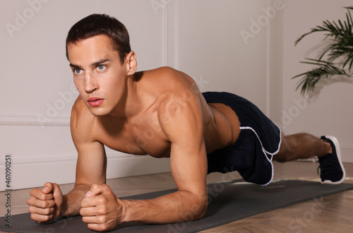 Handsome man doing plank exercise on floor indoors