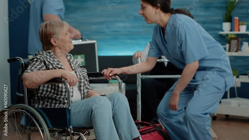 Medical assistant giving support to senior woman with invalidity in nursing home. Retired disabled patient in wheelchair receiving assistance from nurse for recovery and treatment.