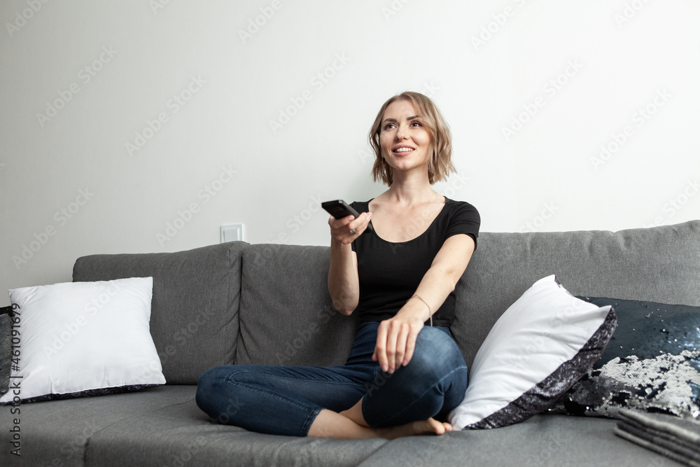 Obraz premium Happy young woman watching tv on sofa