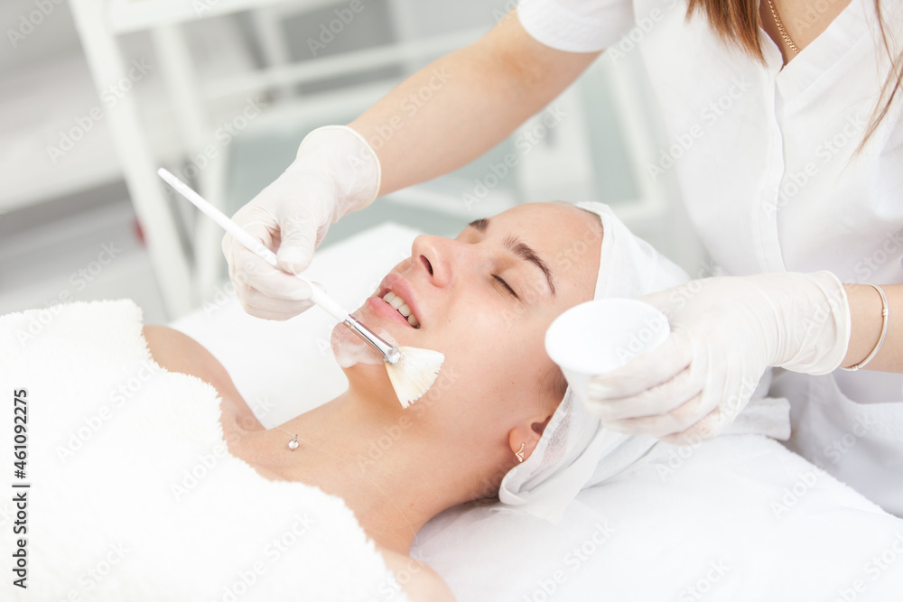 Obraz premium Cosmetological procedures. Beauty salon, doctor in gloves touching face of beautiful woman with closed eyes with brush.