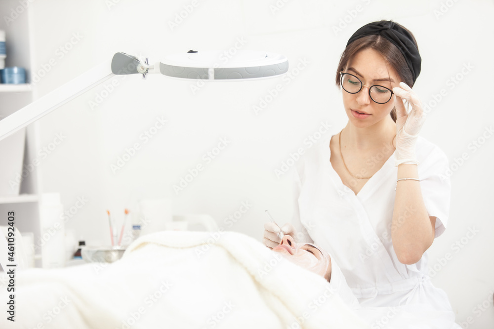 Cute woman beautician makes a cosmetic procedure to patient in beauty salon. Facial skin care Cute woman beautician makes a cosmetic procedure to patient in beauty salon. Facial skin care