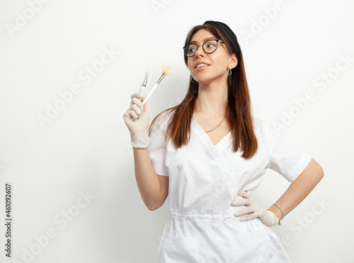 Portrait of young attractive doctor beautician with brushes on white background