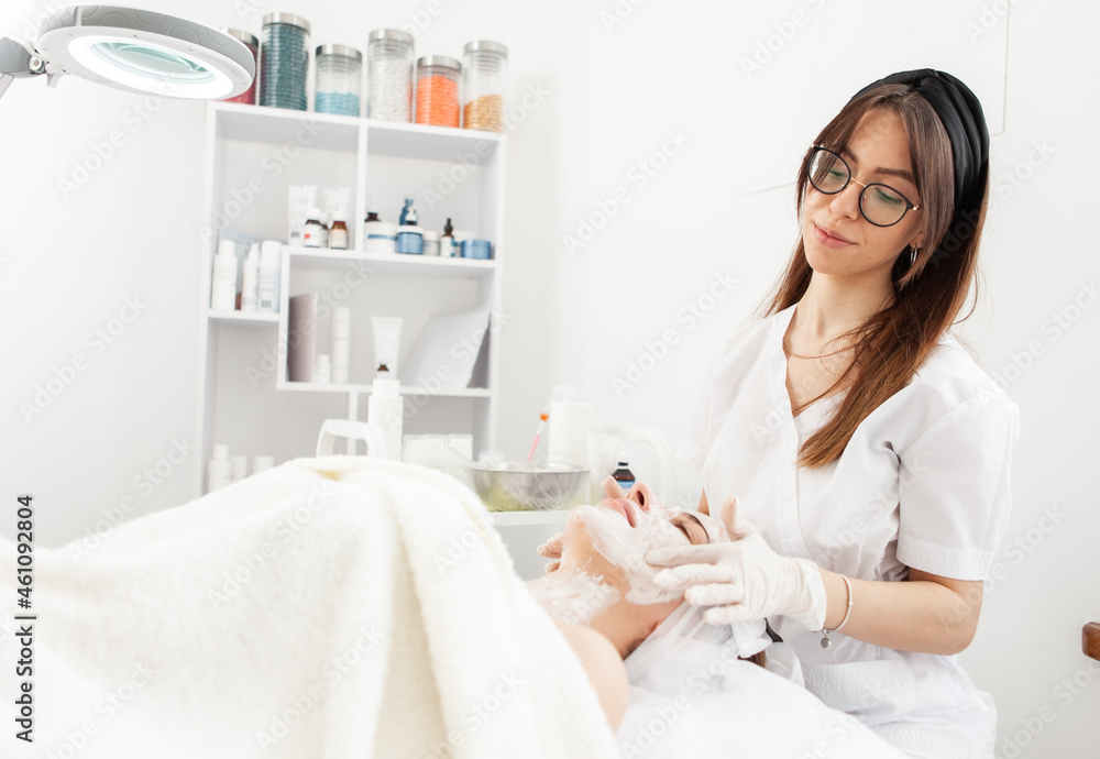 Cosmetological procedures. Beauty salon, doctor in gloves applies mask for beautiful woman with closed eyes Cosmetological procedures. Beauty salon, doctor in gloves applies mask for beautiful woman with closed eyes