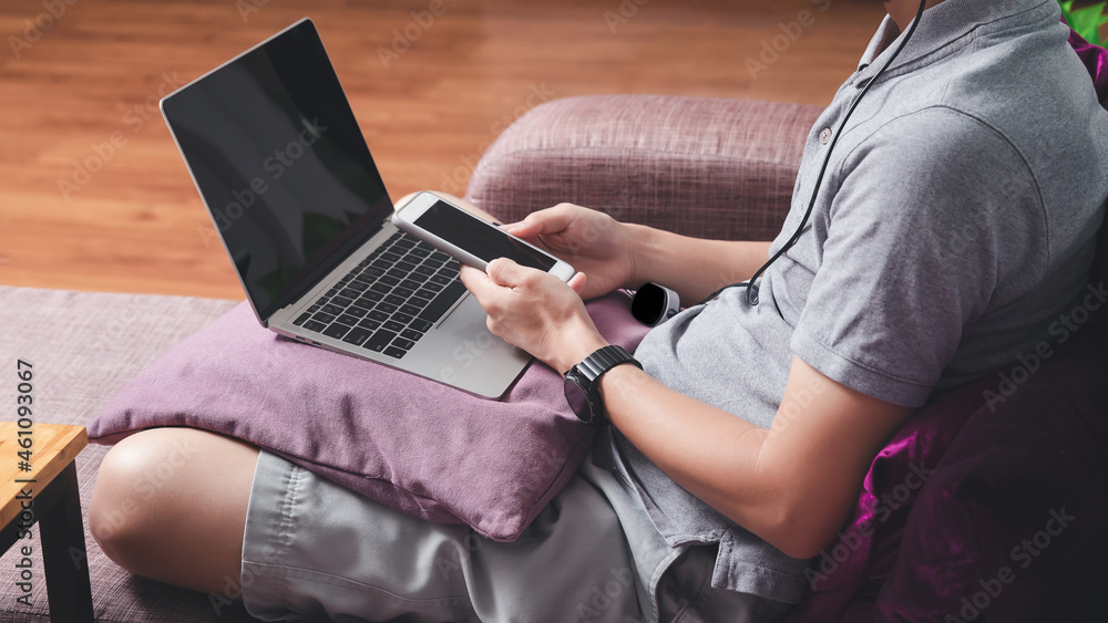 Naklejka premium A man in casual wear using smartphone and laptop while he is working at home office.
