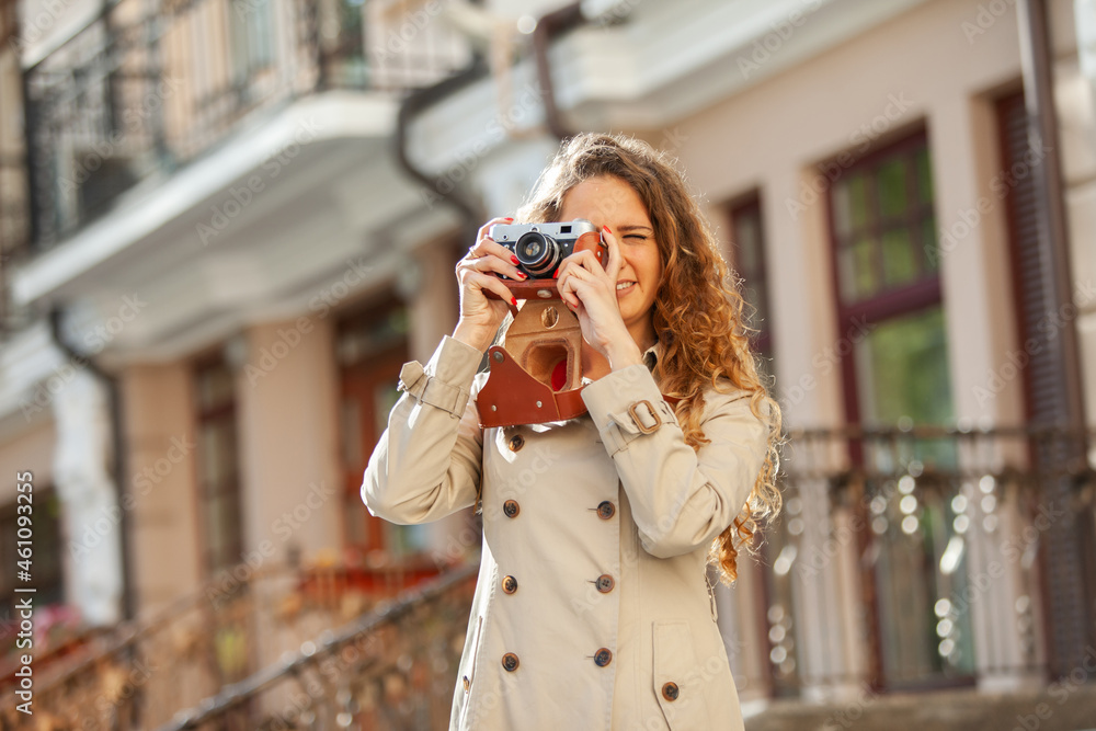 Beautiful curly-haired Caucasian woman with a retro camera in the city. Tourism concept