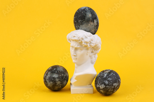 Antique statue with with Gray marble painted Easter eggs on yellow background. Minimalism. Concept art