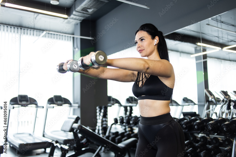 Fitness woman trains shoulder muscles with dumbbells in hands at gym Fitness woman trains shoulder muscles with dumbbells in hands at gym