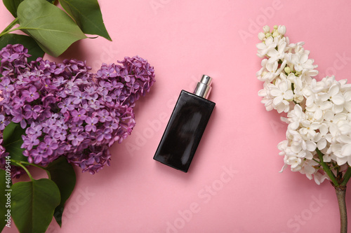 Perfume bottle with branches of blooming lilacs on pink background. Spring, beauty concept. Top view. Flat lay