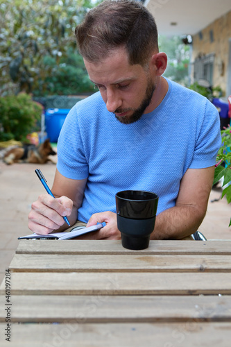 Concentrated young man writing in his diary outdoors
