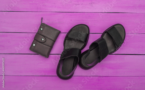 Feminine leather black sandals and wallet on pink wooden background. Top view